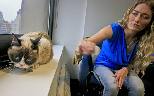 Tabatha Bundesen and her cat, Grumpy Cat, whose real name is Tardar Sauce, pose for a photograph on Friday April 4, 2014, in New York. Bundesen says that Grumpy Cat's permanently grumpy-looking face is due to feline dwarfism. 