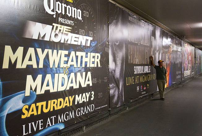 A fan poses by advertisements for May 3rd Floyd Mayweather Jr. vs. Marcos Maidana fight and the April 12th Manny Pacquiao vs. Timothy Bradley fight at the MGM Grand Thursday, April 10, 2014. Top Rank CEO Bob Arum, promoter for boxer Manny Pacquiao, voiced his displeasure at the Mayweather signage during a news conference on Wednesday.