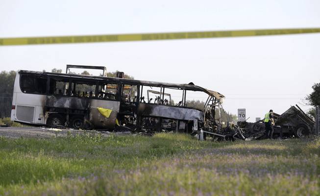A California Highway Patrol Officer looks over the demolished cab of FedEx truck that crashed into a tour bus, at left, on Interstate 5 Thursday in Orland, Calif., Friday, April 11, 2014. At least ten people were killed and dozens injured in the fiery crash between the truck and a bus carrying high school students on a visit to a Northern California College.