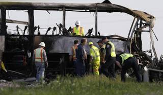 Officials and California Highway Patrol Officers look over the remains of a tour bus that was struck by a FedEx truck on Interstate 5 Thursday in Orland, Calif., Friday, April 11, 2014. At least ten people were killed and dozens injured in the fiery crash between the truck and a bus carrying high school students on a visit to a Northern California College.