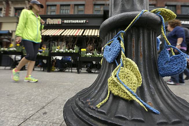 A passerby walks past yellow-and-blue crocheted hearts that hang from a lamp post in front of the Forum restaurant near the finish line of the Boston Marathon on Monday, April 14, 2014, in Boston. 