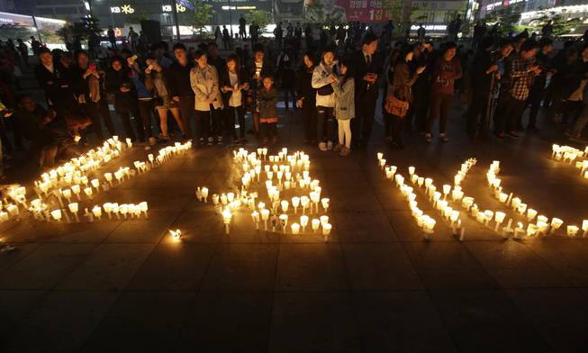 People stand near candles during a vigil for the safe return of passengers of the sunken ferry Sewol in Ansan, South Korea, Thursday, April 24, 2014.