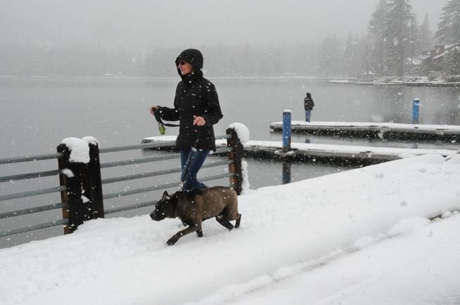Shelley Long and her dog Brew enjoy a lakefront walk near their home as snow falls Friday, April 25, 2014, at Donner Lake in Truckee, Calif. A late-season storm brought several inches of snow to the Sierra Nevada, making for a pretty day but snarling traffic on nearby Interstate 80. In the background, a fisherman tries his luck.