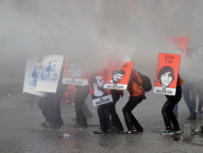 Protesters hold posters with images of the victims of the last year's protests as riot police use water cannons and teargas to disperse thousands of people trying to reach the city's main Taksim Square to celebrate May Day in Istanbul, Turkey, Thursday, May 1, 2014. Clashes erupted between May Day demonstrators and riot police as crowds determined to defy a government ban tried to march to the city's iconic Taksim Square. Security forces pushed back demonstrators with water cannons and tear gas. 