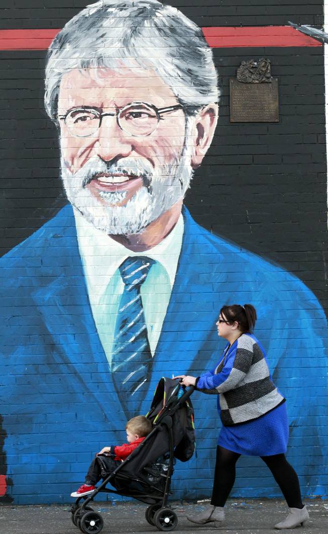 A woman and child make their way past a newly painted mural of Gerry Adams on the Falls Road, West Belfast, Northern Ireland, Friday, May, 2, 2014. Police continue to question the Sinn Fein leader Gerry Adams at Antrim police station about the 1972 murder of Jean McConville.