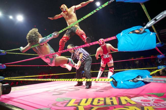 In this Feb. 12, 2014, photo, wrestler Niebla Roja, top, flies over referee Platainitos, to land on wrestler Cassandro, left, during a performance at Lucha VaVoom's Valentine’s show at The Mayan Theatre downtown Los Angeles. At right, wrestler, Dr. Maldad. The esoteric hybrid of American burlesque and Mexican wrestling is an outrageous hit.