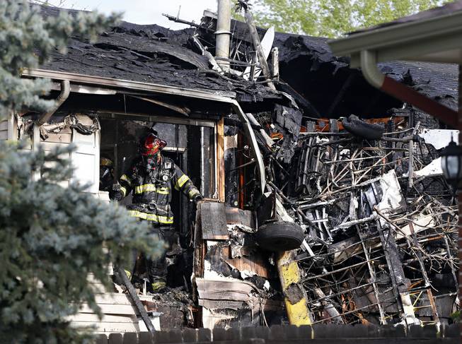 A firefighter looks for hotspots in the debris after his team put out a fire at the scene where a small plane crashed into a home in Northglenn, Colo., Monday, May 5, 2014. 
