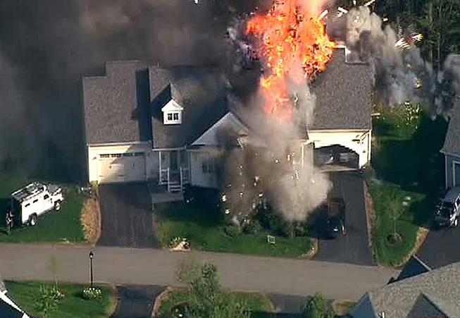In this frame grab from television helicopter video, a police SWAT team, left, is parked on the lawn of a home in Brentwood, N.H., as it explodes in flames, Monday May 12, 2014. Shots were fired just before the fire, which involved a police officer.