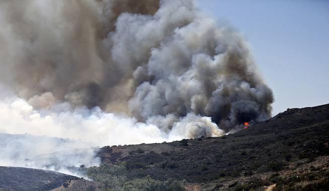 Billowing smoke rises from flames as firefighters begin the trek up the hills to battle a wild fire, Tuesday, May 13, 2014, in San Diego. 