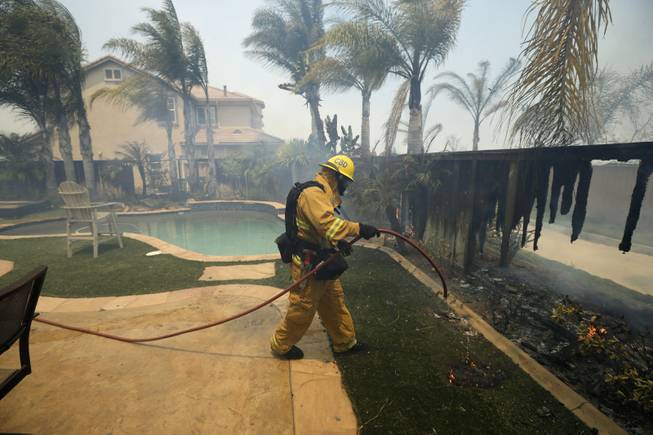 A Firefighter puts water on a house fence during a wildfire Wednesday, May 14, 2014, in Carlsbad, Calif. More wildfires broke out Wednesday in San Diego County  threatening homes in Carlsbad and forcing the evacuations of military housing and an elementary school at Camp Pendleton  as Southern California is in the grip of a heat wave. 