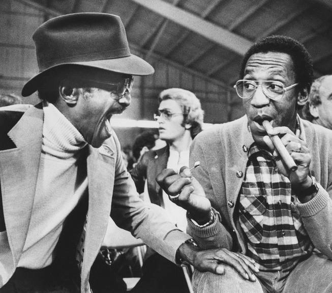 Entertainer Sammy Davis Jr. shares a laugh with comedian Bill Cosby right, as he lights his cigar while attending the light heavyweight fight in Las Vegas Saturday , February 27, 1979 . The scheduled fight between Mike Rossman and Victor Galindez was indefinitly postponed. 