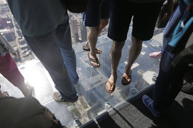 People stand on the floor of one of four transparent ledges that jut out from the 103rd floor of the Willis Tower in Chicago on Thursday, May 29, 2014. 