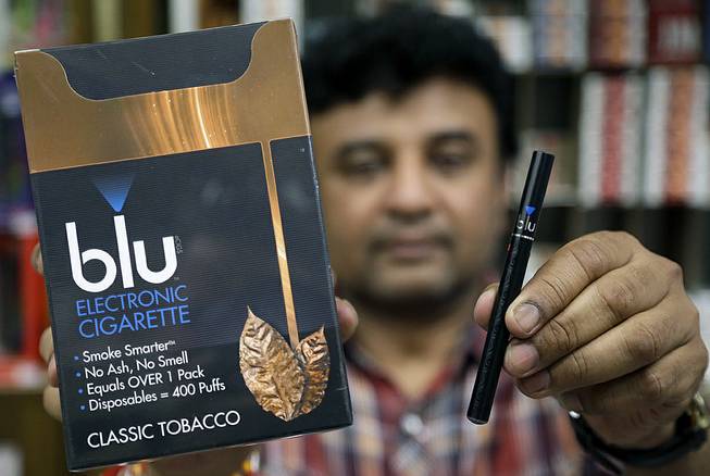 Sales clerk Sam Patel, of Waltham, Mass., displays a blu e-cigarette, right, and a container of the e-cigarettes, left, at a shop, Wednesday, May 21, 2014, in Brookline, Mass. 