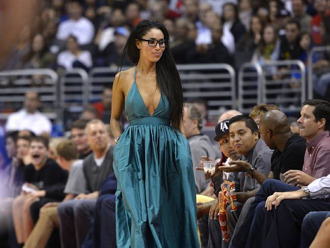 In this photo taken on Friday, Oct. 25, 2013, V. Stiviano, left, walks to her seat as she watches the Clippers play the Sacramento Kings during the first half of an NBA basketball game in Los Angeles. 