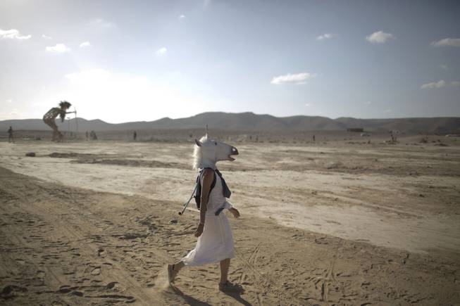 In this photo taken Friday, June 6, 2014, An Israeli woman wears a unicorn mask as she walks in the playa during Israelis first Midburn festival in the desert near the Israeli kibbutz of Sde Boker.