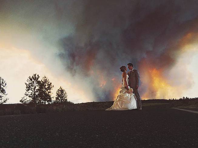 Newlyweds Michael Wolber and April Hartley pose for a picture near Bend, Ore., as a wildfire burns in the background, Saturday, June 7, 2014. Because of the approaching fire, the minister conducted an abbreviated ceremony and the wedding party was evacuated to a downtown Bend park for the reception.