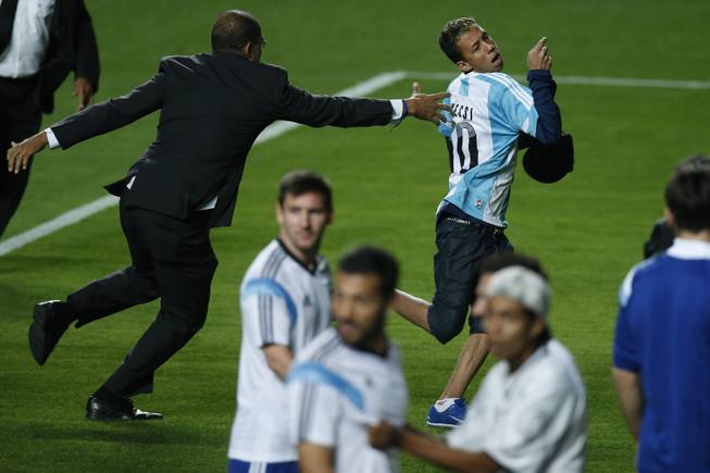 A security guard fails to stop a fan who invaded the pitch wearing an Argentine jersey, top, as Argentina's Lionel Messi, center, and other players look on at the end of a training session at Independencia Stadium in Belo Horizonte, Brazil, Wednesday, June 11, 2014. Argentina will play in group F of the Brazil 2014 soccer World Cup. 