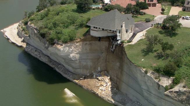 In this image taken from video provided Thursday, June 12, 2014, by WFAA.Com, a luxury house teeters on a cliff about 75 feet above Lake Whitney in Whitney, Texas.