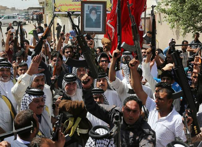 In this Saturday, June 14, 2014, photo, Iraqi Shiite tribal fighters raise their weapons and chant slogans against the al-Qaida-inspired Islamic State of Iraq and the Levant (ISIL) in Baghdad's Sadr city, Iraq. Emboldened by a call to arms by the top Shiite cleric, Iranian-backed militias have moved quickly to the center of Iraq’s political landscape, spearheading what its Shiite majority sees as a fight for survival against Sunni militants who control of large swaths of territory north of Baghdad. The poster at top depicts Grand Ayatollah Mohammed Sadiq al-Sadr, the late father of Shiite cleric Muqtada al-Sadr.