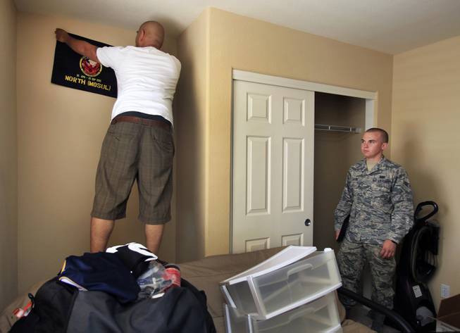 Rommel Delmundo, stationed at Nellis AFB, takes down a unit flag from his bedroom as he and his family ready for another military move Monday, June 16, 2014.  Jake Carter with Nellis AFB public affairs assists to ensure things go smoothly.