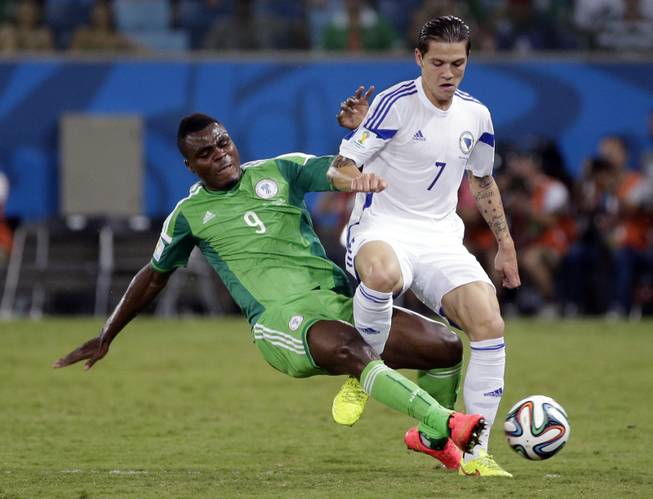 Nigeria's Emmanuel Emenike slides into Bosnia-Herzegovina's Muhamed Besic to kick the ball away during the a World Cup soccer match at the Arena Pantanal in Cuiaba, Brazil, on Saturday, June 21, 2014.