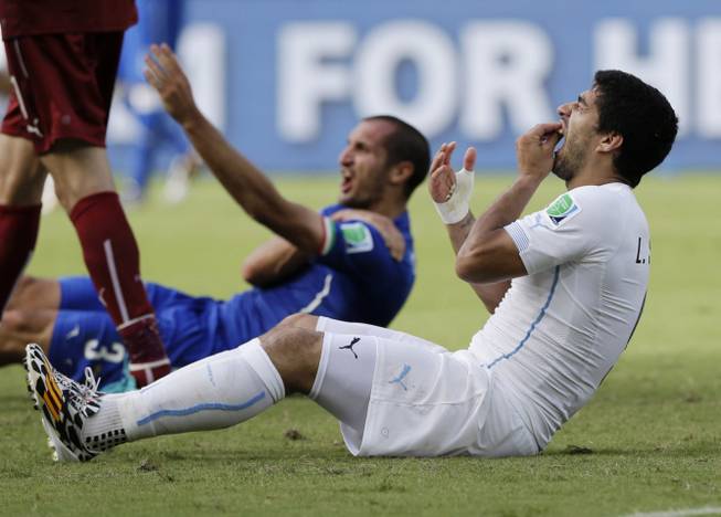In this June 24, 2014, file photo, Uruguay's Luis Suarez holds his teeth after biting Italy's Giorgio Chiellini's shoulder during the group D World Cup soccer match between Italy and Uruguay at the Arena das Dunas in Natal, Brazil. On Thursday, June 26, 2014, FIFA banned Suarez for 9 games and 4 months for biting his opponent at the World Cup.