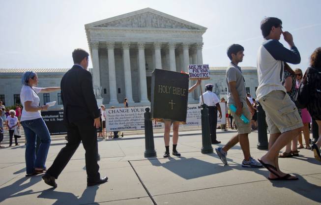 A demonstrator dressed as the 'Bible' stands outside the Supreme Court in Washington, Monday, June 30, 2014, awaiting the court's decision on the Hobby Lobby case. The Supreme Court says corporations can hold religious objections that allow them to opt out of the new health law requirement that they cover contraceptives for women.