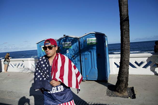 A fan of the U.S. national soccer team walks by the seaside with a U.S. flag draped over his shoulders, in Salvador, Brazil, Monday, June 30, 2014. Salvador is one of the host cities of the FIFA 2014 Soccer World Cup. 