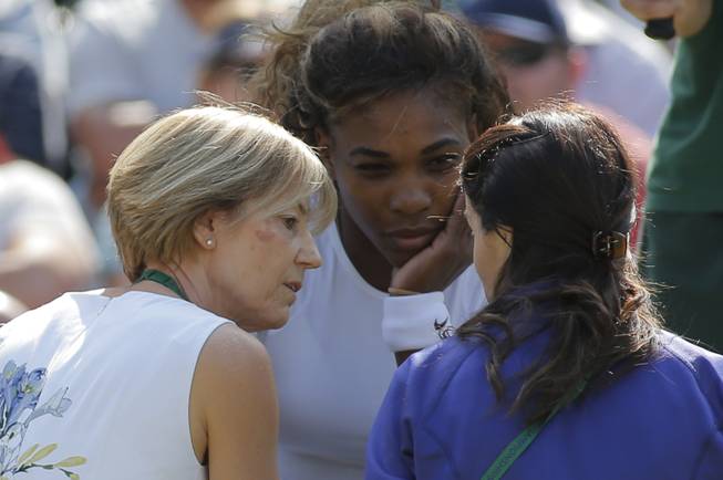 Court officials talk to Serena Williams of the U.S as she and Venus Williams retire after 3 games from their women's doubles match against Kristina Barrois of Germany and Stefanie Voegele of Switzerland at the All England Lawn Tennis Championships in Wimbledon, London, Tuesday July 1, 2014.