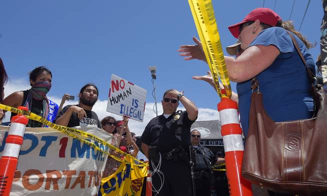 Demonstrators from opposing sides confront each other while being separated by Murrieta police officers, Friday, July 4, 2014, outside a U.S. Border Patrol station in Murrieta, Calif. Demonstrators on both sides of the immigration debate had gathered where the agency was foiled earlier this week in an attempt to bus in and process some of the immigrants who have flooded the Texas border with Mexico.