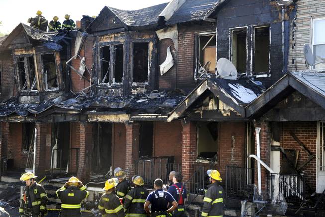 Firefighters work at a scene of a fire that that raced through a row of two-story homes in southwest Philadelphia on Saturday, July 5, 2014. The fire that killed three 4-year-olds and a baby, engulfing at least 10 houses, may have started in a couch on a porch, officials said.