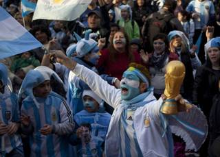 An Argentina soccer fan cheers while holding a replica of the World Cup trophy before a World Cup semifinal match between Argentina against Netherlands, on a street where an outdoor screen has been set for viewing, in Buenos Aires, Argentina, Wednesday, July 9, 2014. 