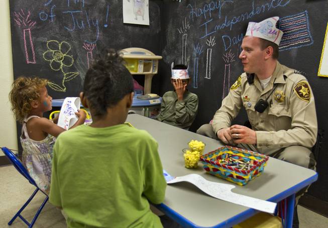 Metro Police Officer Gordie Bush joins Brooklyn, 3, Anthony, 6, and Christian Bannister, 8, in making paper and crayon hats at the Sherman Gardens Youth Center on Thursday, July 3, 2014.