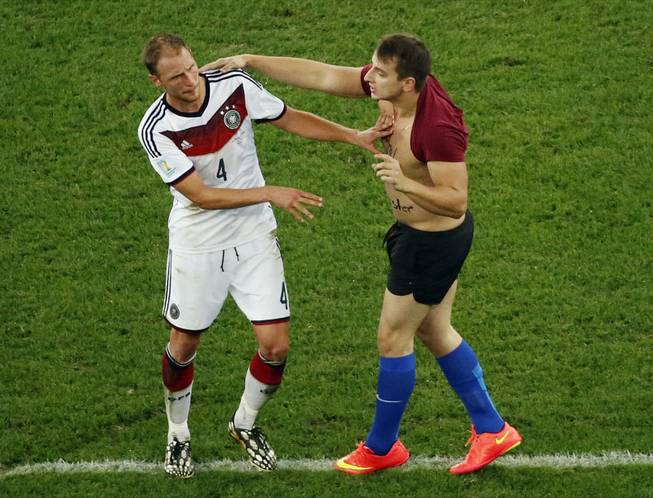 Germany's Benedikt Hoewedes faces a man who run into the pitch during the World Cup final soccer match between Germany and Argentina at the Maracana Stadium in Rio de Janeiro, Brazil, Sunday, July 13, 2014.