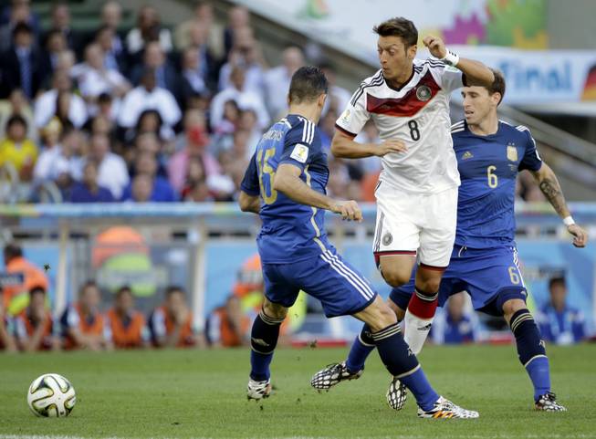Germany's Mesut Ozil tries to get past his defenders Argentina's Martin Demichelis and Lucas Biglia (6) during the World Cup final soccer match between Germany and Argentina at the Maracana Stadium in Rio de Janeiro, Brazil, Sunday, July 13, 2014.