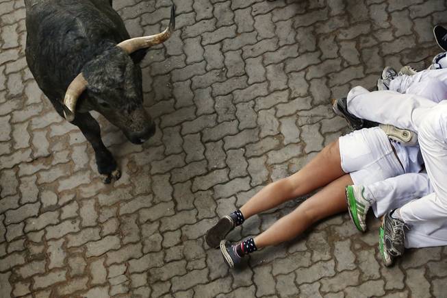 AP10ThingsToSee - Fallen revelers lie on the ground as a fighting bull runs by during the running of the bulls at the San Fermin festival, in Pamplona, Spain, Sunday, July 13, 2014. 