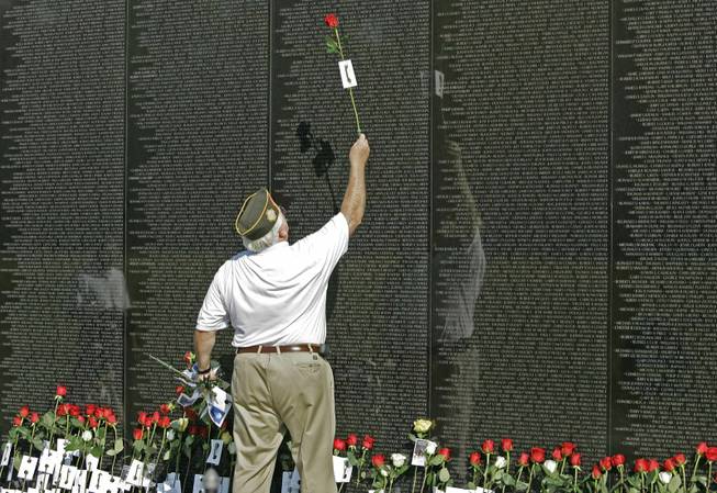 Maj. Wayne Witter, of Dunwoody, Ga., holds a red rose in 2007 as he touches the name of a fallen comrade at the Vietnam Veterans Memorial in Washington. The names of 74 sailors who died in a ship collision in 1969 haven’t been added because their ship was outside the official war zone.