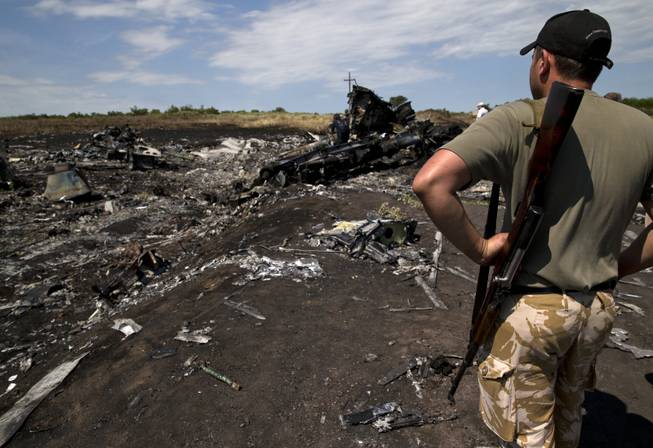 An armed man looks at charred debris at the crash site of Malaysia Airlines Flight 17 near the village of Hrabove, eastern Ukraine, Sunday, July 20, 2014. Armed rebels forced emergency workers to hand over all 196 bodies recovered from the Malaysia Airlines crash site and had them loaded Sunday onto refrigerated train cars bound for a rebel-held city, Ukrainian officials and monitors said.
