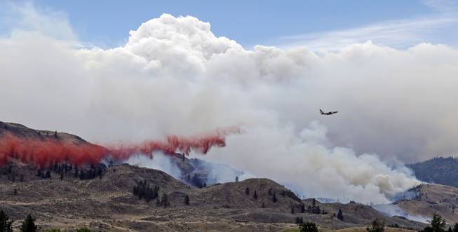 A DC-10 air tanker drops fire retardant over a wildfire as smoke rises and billows behind Saturday, July 19, 2014, near Carlton, Wash. A wind-driven, lightning-caused wildfire racing through rural north-central Washington destroyed about 100 homes Thursday and Friday, leaving behind solitary brick chimneys and burned-out automobiles as it blackened hundreds of square miles in the scenic Methow Valley northeast of Seattle.