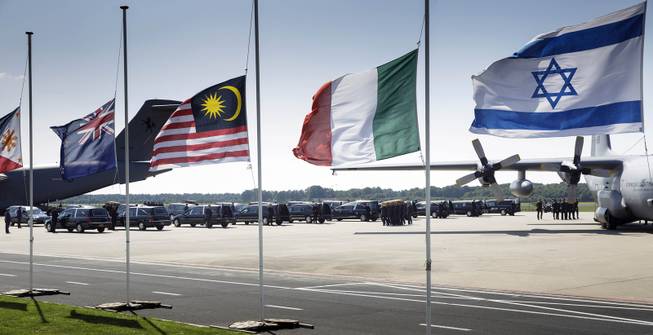 Flags fly half-staff as pallbearers carry a coffin out of a military transport plane during a ceremony to mark the return of the first bodies, of passengers and crew killed in the downing of Malaysia Airlines Flight 17, from Ukraine at Eindhoven military air base, Wednesday, July 23, 2014. After being removed from the planes, the bodies are to be taken in a convoy of hearses to a military barracks in the central city of Hilversum, where forensic experts will begin the painstaking task of identifying the bodies and returning them to their loved ones. Flags from left: Philippines, New Zealand, Malaysia, Italy and Israel. 