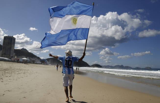 In this July 14, 2014, file photo, an Argentina soccer fan waves Argentina's national flag the morning after his team was defeated by Germany at the World Cup final, on Copacabana beach in Rio de Janeiro, Brazil. Local media reports say tens of thousands of Argentine fans have remained in the country after the tournament ended. But the prospect of a large number of foreigners selling handicrafts, juggling at intersections for handouts or relying on government social services for poor Brazilians has officials worried.