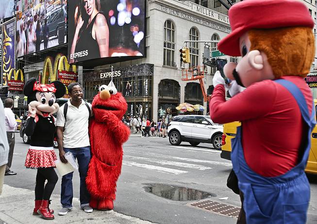 A visitor to Times Square stands for photos with costumed characters Monday, July 28, 2014, in New York. New York Mayor Bill de Blasio said Monday that he believes the people wearing character costumes in Times Square should be licensed and regulated.