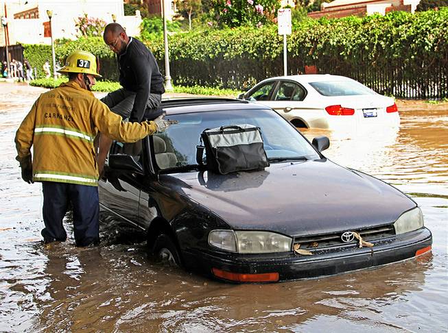A Los Angeles firefighter helps a driver whose car became stranded on Sunset Boulevard after a 30-inch water main broke and sent water flooding down Sunset and onto the UCLA campus in the Westwood section of Los Angeles Tuesday, July 29, 2014. 