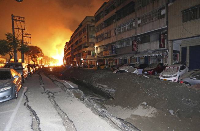 Tossed vehicles line an destroyed street as flames continue to burn from multiple explosions from an underground gas leak in Kaohsiung, Taiwan, early Friday, Aug. 1, 2014. A massive gas leakage early Friday caused five explosions that killed several people and injured over 200 in the southern Taiwan port city of Kaohsiung.