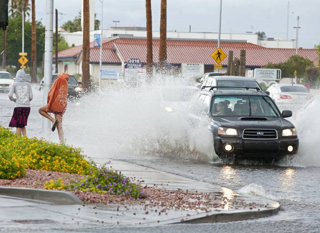 A pedestrian attempts to lean away from the wake of a passing car after an afternoon downpour temporarily turned Charleston Boulevard into a rushing river on Monday afternoon.