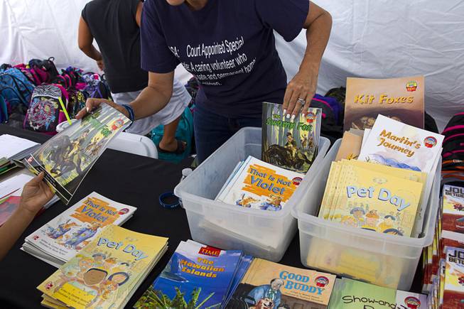 A volunteer hands out books during a special back-to-school event for foster children at Square Salon, 1225 South Fort Apache Blvd., during a Sunday, August 10, 2014. The event was sponsored by the CASA Foundation, a local non-profit organization, in partnership with Square Salon and other organizations.