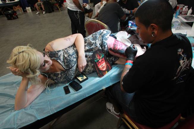 Hova Villasenor from Artistic Element inks a design on the thigh of Lara Ashton during the 3rd annual Art-N-Ink Tattoo Festival Saturday, Aug. 9, 2014 at the South Point.