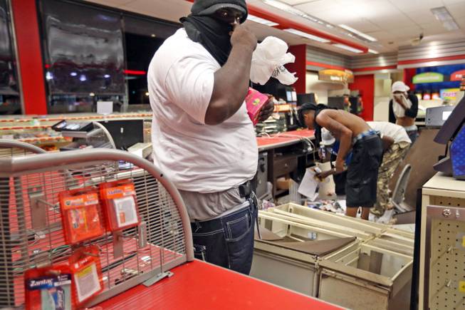 People are seen in a store Sunday, Aug. 10, 2014, in Ferguson, Mo. A few thousand people crammed a suburban St. Louis street Sunday night at a vigil for unarmed 18-year-old Michael Brown, shot and killed by a police officer, while afterward several car windows were smashed and stores were looted as people carried away armloads of goods as witnessed by an an Associated Press reporter.