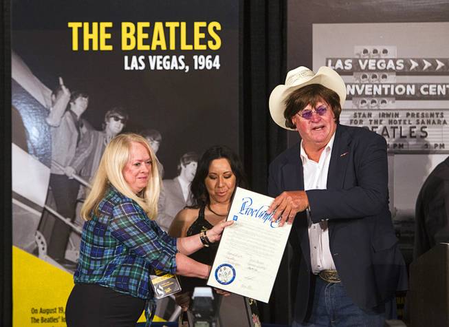 Clark County Commissioner Tom Collins, wearing a Beatles wig and glasses, gives out proclamations to sisters Cheryl, left, and Kim McDonald during a news conference in the lobby of the Las Vegas Convention Center Tuesday, Aug. 12, 2014. Their father Herb McDonald, a Las Vegas publicist, was involved in bringing the Beatles to Las Vegas for a concert in 1964. A multi-media exhibition commemorating the concert will be on display in the lobby of the LVCC through Oct. 27.