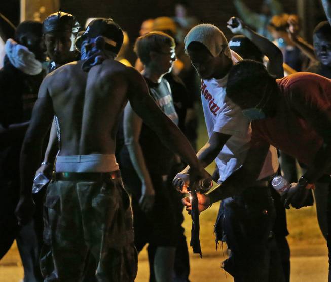 Protesters try unsuccessfully to light a Molotov cocktail, Wednesday, Aug. 13, 2014, in Ferguson, Mo. Protests in the St. Louis suburb rocked by racial unrest since a white police officer shot an unarmed black teenager to death turned violent Wednesday night, with people lobbing molotov cocktails at police who responded with smoke bombs and tear gas to disperse the crowd.
